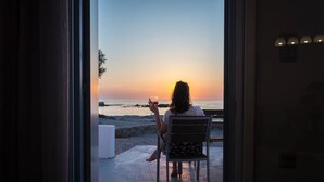 Une personne assise près d’une fenêtre, d’où l’on peut admirer le coucher de soleil sur la plage.