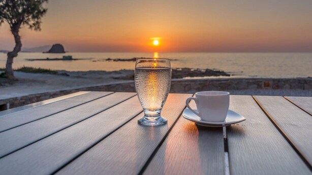 Une table avec un verre d’eau et une tasse, placée devant un paysage au coucher du soleil.