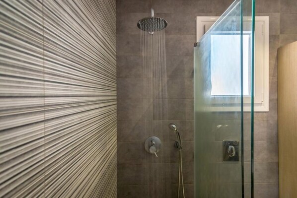 Eine Dusche mit Glastür, Regendusche und einem Fenster darüber.