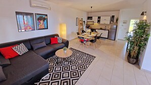 Una sala moderna con sofá, una mesa de centro y un tapete estampado. Se ve un comedor con sillas y una mesa al fondo.
