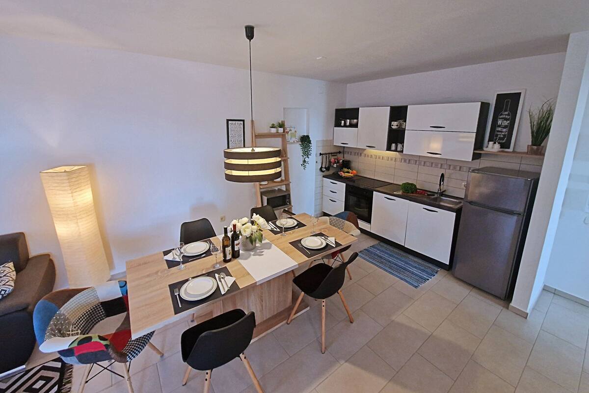 A modern kitchen with white cabinets, a stainless steel refrigerator, and a dining area with a wooden table and black chairs.
