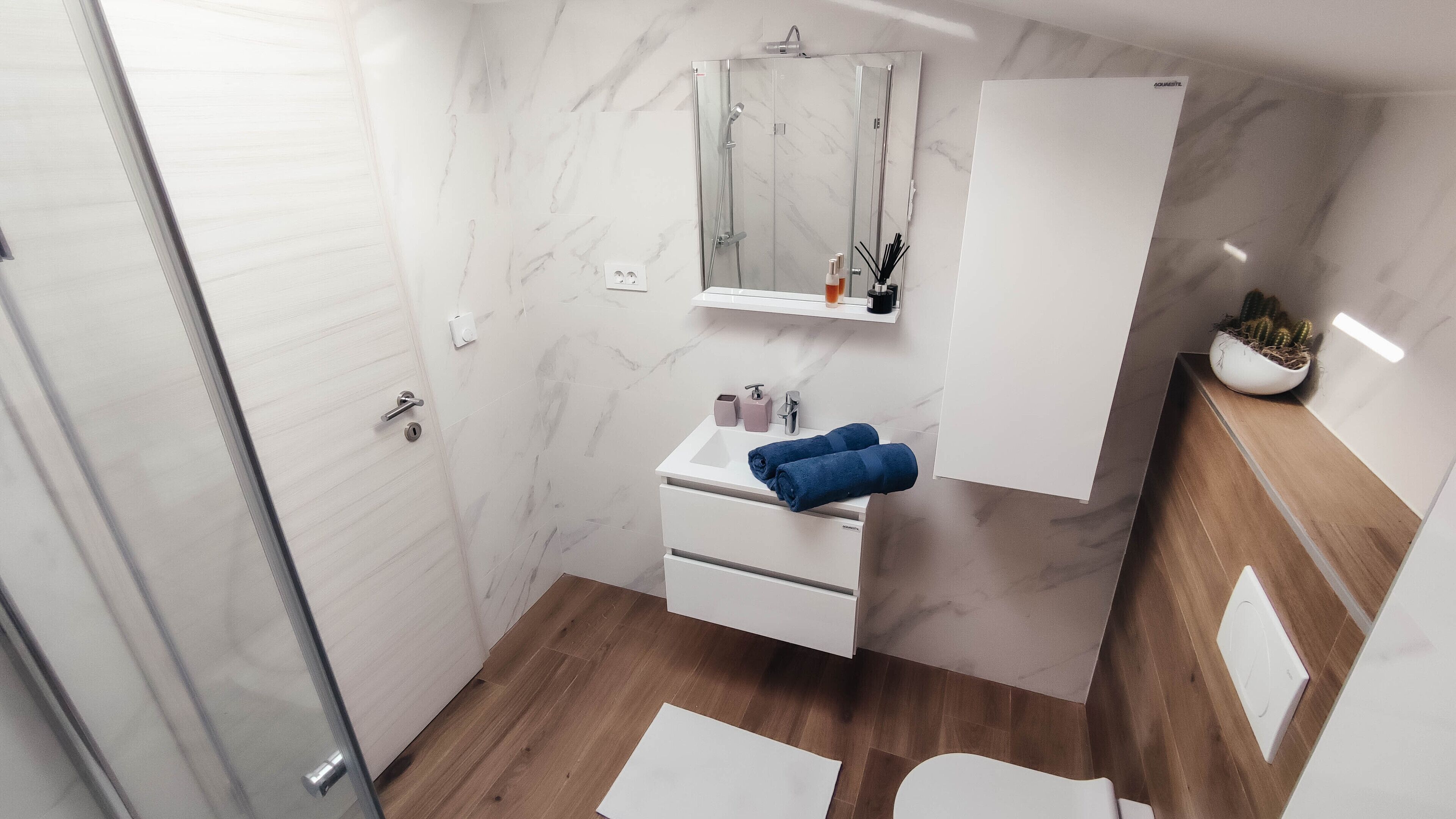 A modern bathroom with a glass shower enclosure, a white sink with a mirror above, and a wooden vanity.