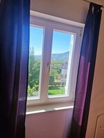 Una habitación con ventana que da a un paisaje verde y un edificio con tejado de tejas.