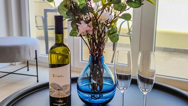 Una mesa con una botella de vino, un florero con flores, dos copas y un plato de fresas.
