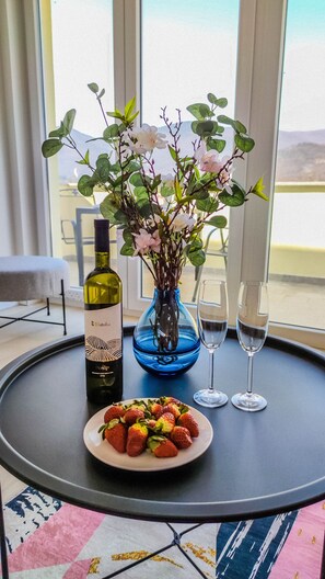 Un tavolo con una bottiglia di vino, un vaso di fiori, due bicchieri e un piatto di fragole.