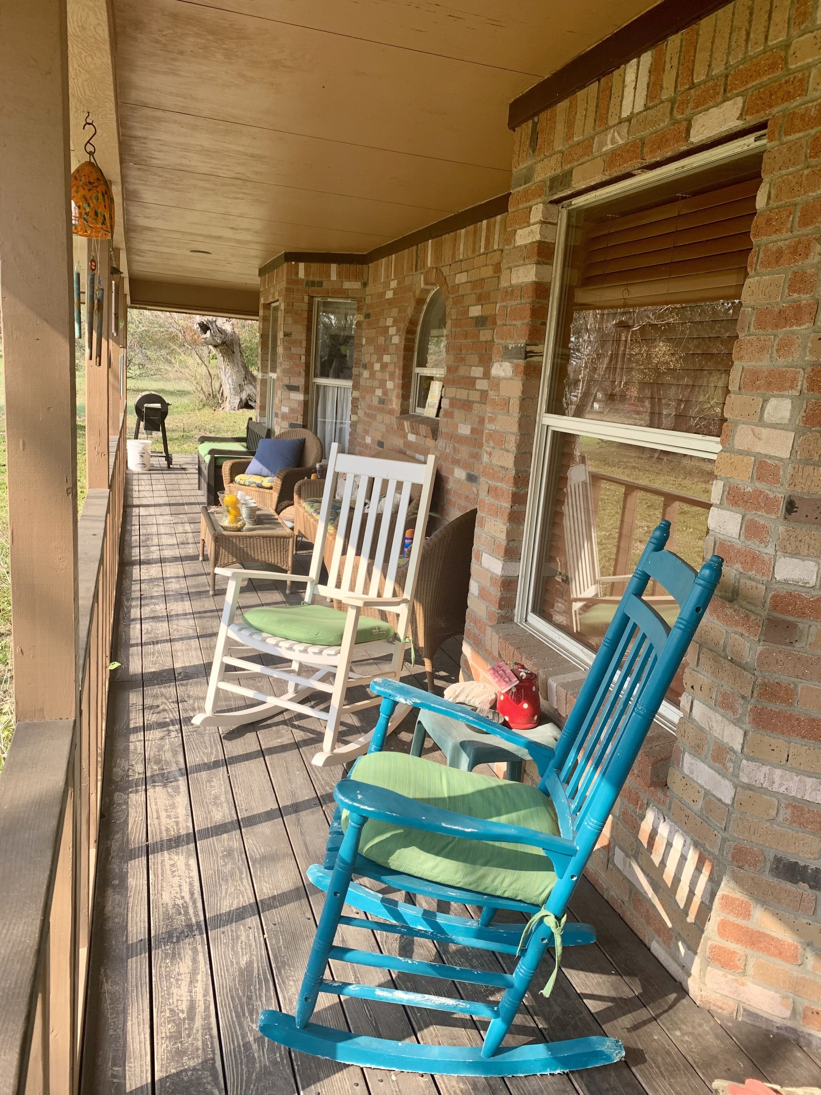Een houten terras met schommelstoelen en een tafel, bakstenen muren en een overdekte veranda.