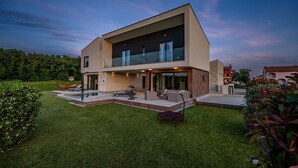 Une maison moderne à deux étages, dotée d’une piscine, d’un espace de détente extérieur et d’une pelouse bien entretenue.