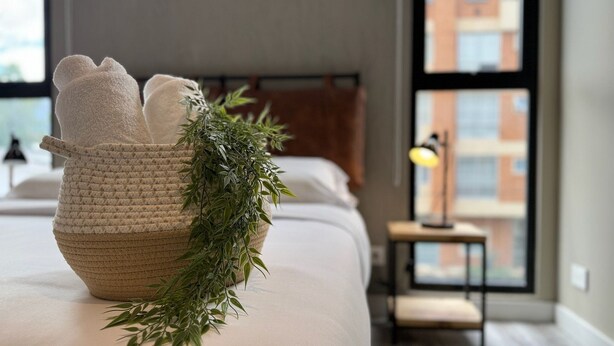 A neatly made bed with a woven basket containing towels and a green plant.