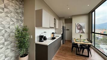 A modern kitchen with a central island, a dining area with a wooden table, and a large window offering a city view.