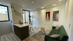A modern living room with a green sofa, a small round coffee table, and a kitchen area with a white countertop and a sink.