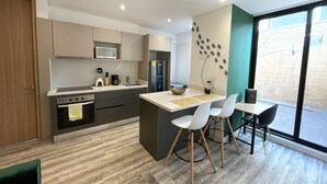 A modern kitchen with a central island, white chairs, and a large window.
