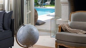 Un salon avec une cheminée, un globe terrestre et une piscine visible à travers une porte ouverte.