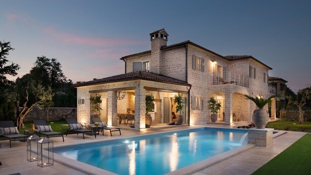 Une maison en pierre à deux étages, dotée d’une piscine, d’un espace salon extérieur et d’une terrasse bien éclairée.
