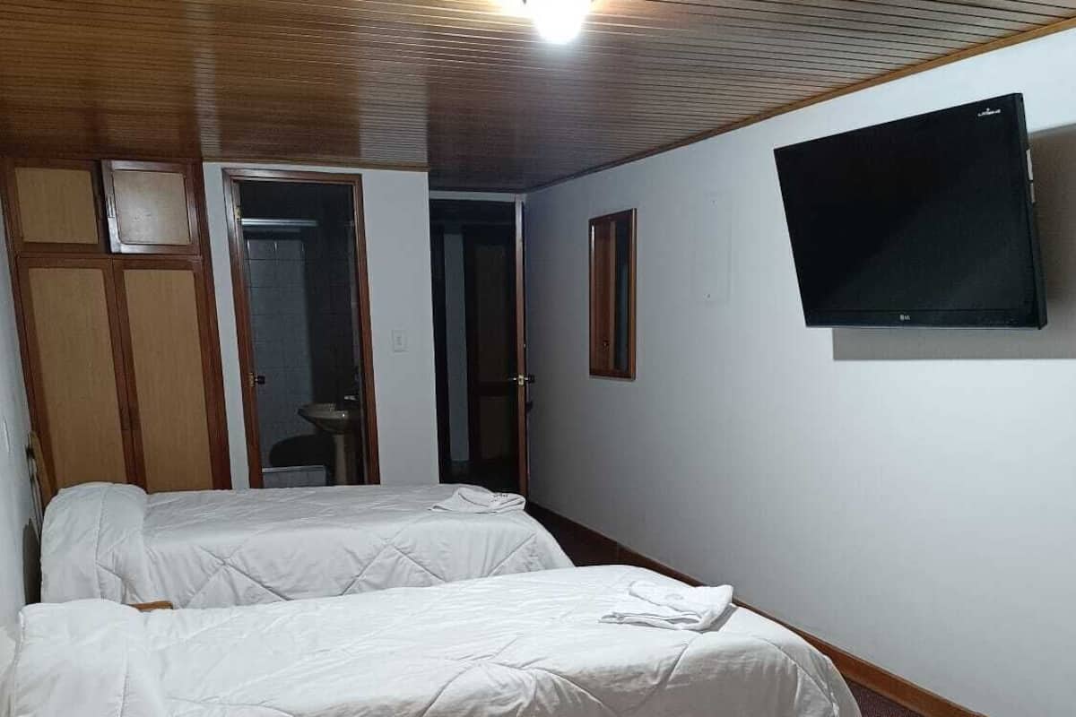 Ein Zimmer mit zwei Betten, einem Fernseher an der Wand und einer Holzbalkendecke.