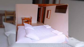 A neatly made bed with pillows and a folded towel, a wooden chair, and a small table in a room with a door leading to another space.