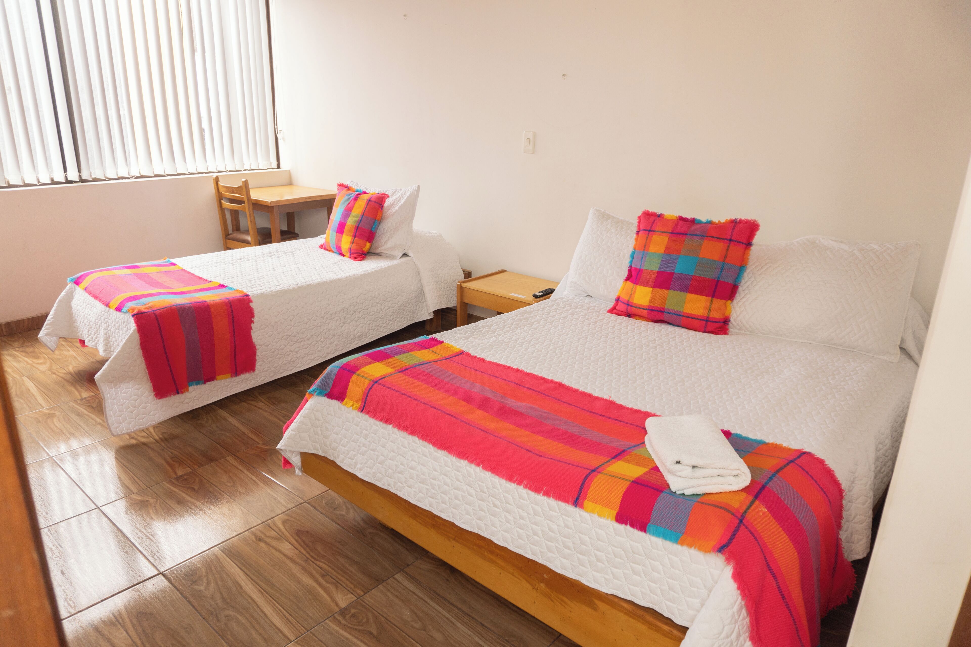 A hotel room with two beds, each with a colorful blanket and pillow, a wooden nightstand, and a chair.