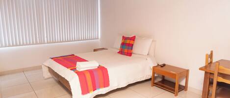 A bedroom with a bed, a bedside table, a chair, and a window with blinds.