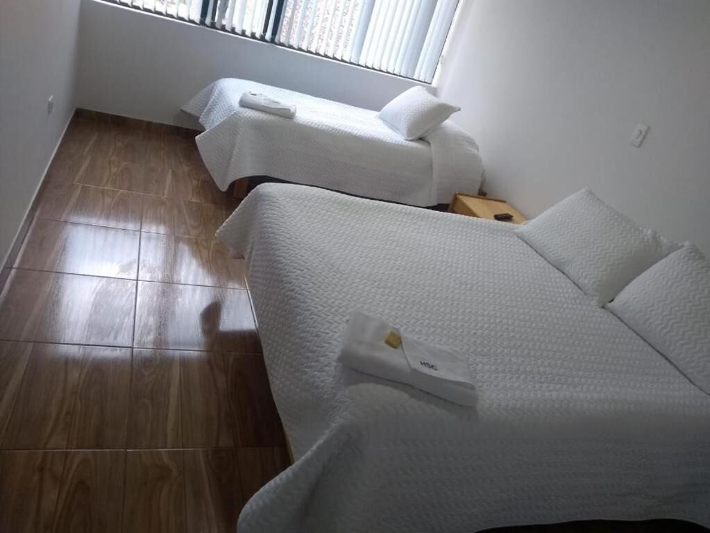 Una habitación con dos camas, piso de madera y una ventana con persianas.