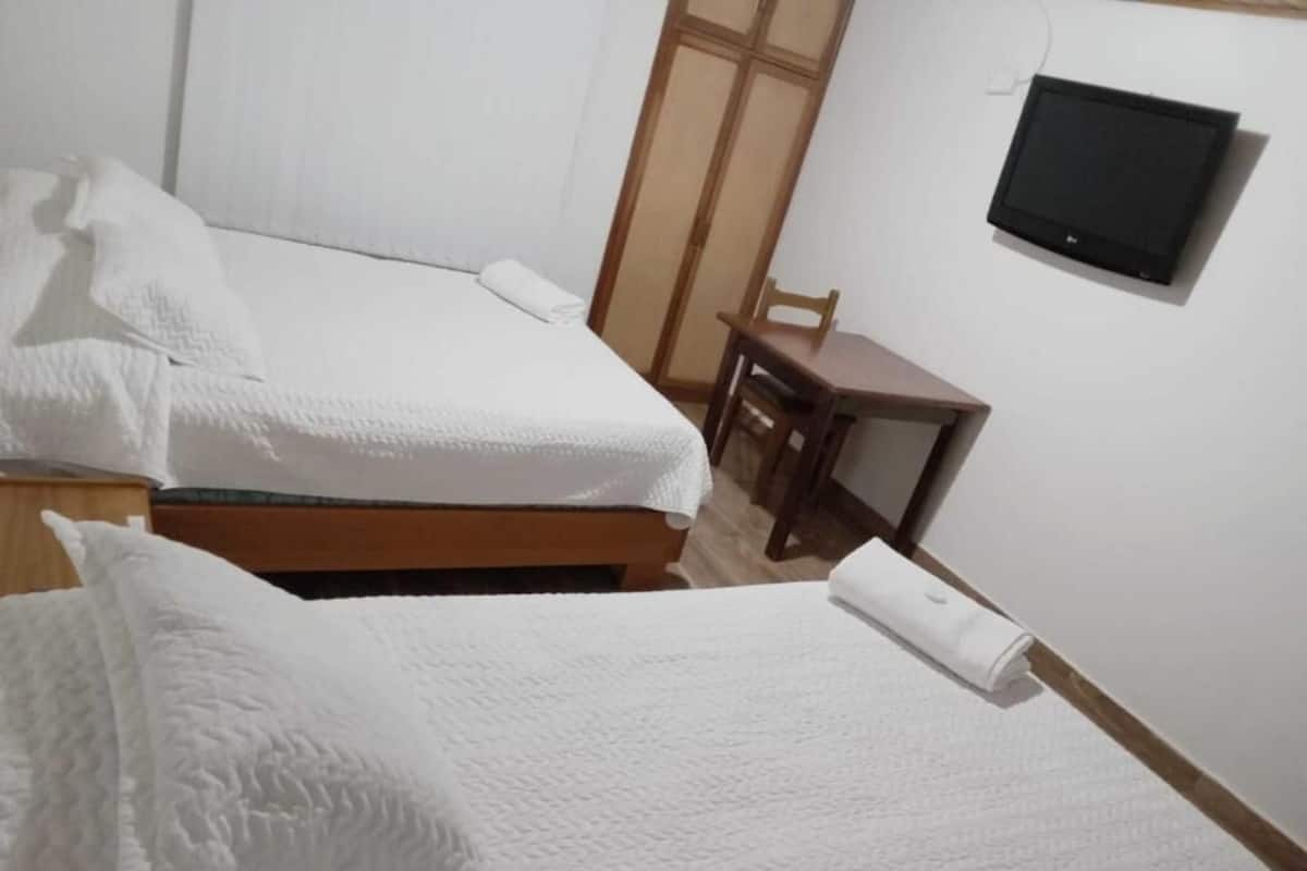 Ein Zimmer mit zwei Betten, einem Holztisch, einem Stuhl und einem Fernseher an der Wand.