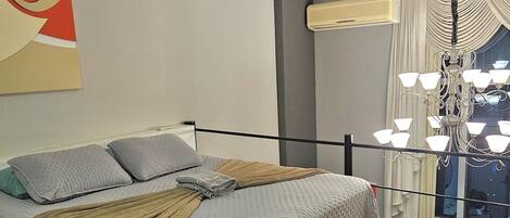 A bedroom with a bed, a chandelier, a window with curtains, and an air conditioning unit.