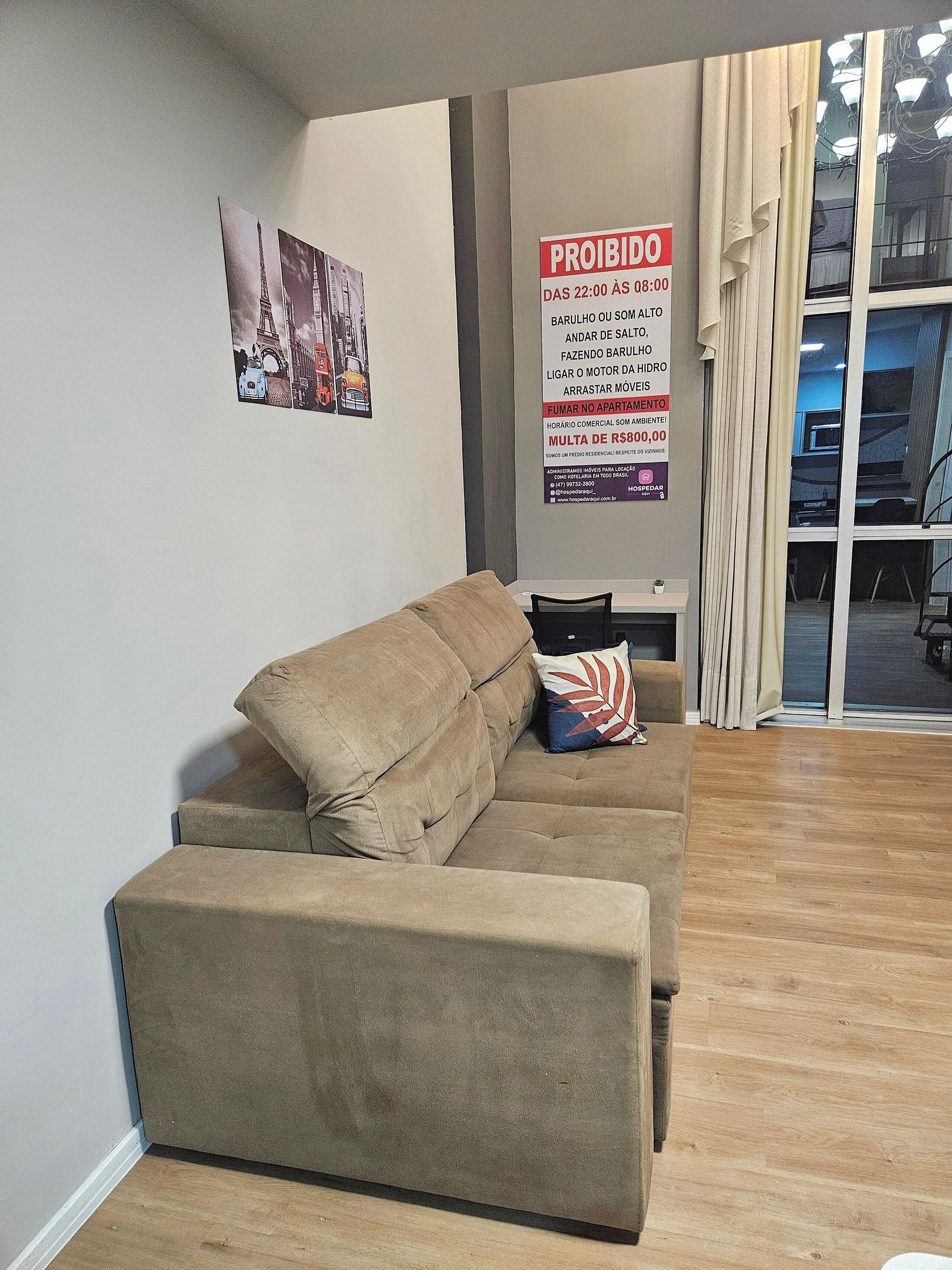 A living room with a sofa and a small table, a poster on the wall, and a window with curtains.