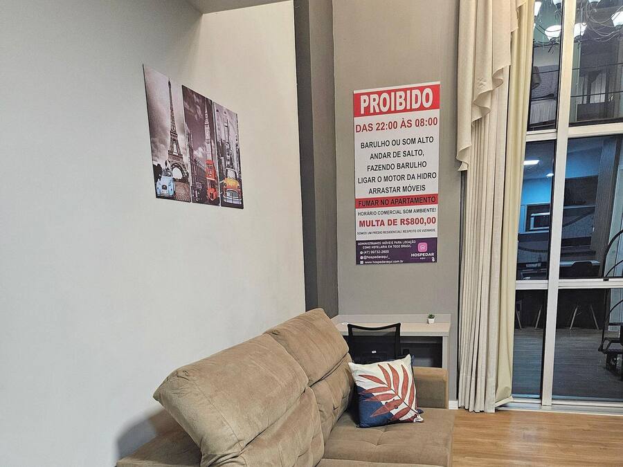 Una sala de estar con un sofá y una mesita, un cartel en la pared y una ventana con cortinas.