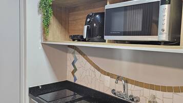Uma cozinha com bancada preta, pia de aço inoxidável, micro-ondas e cafeteira.