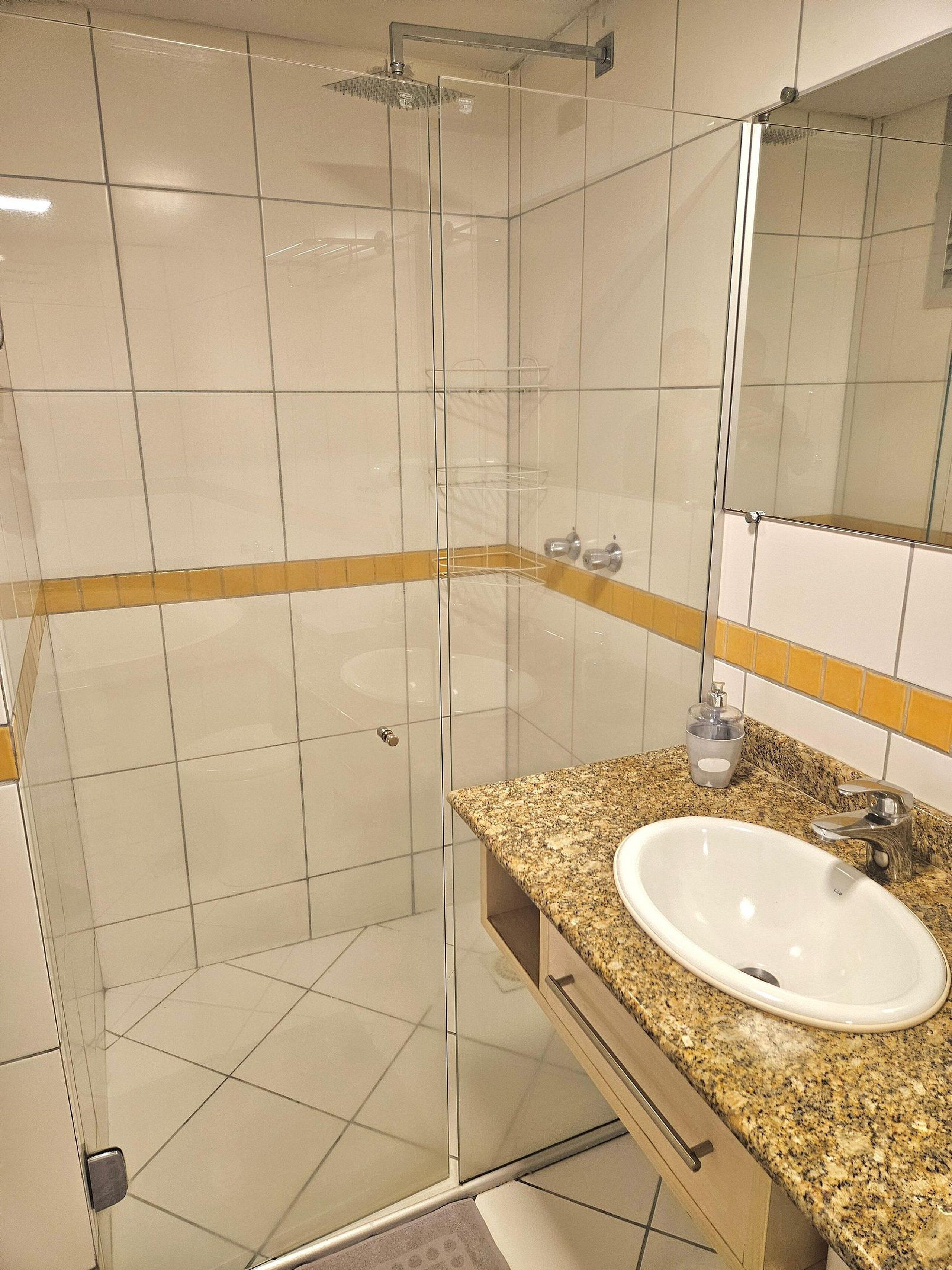 A bathroom with a glass-enclosed shower, a granite countertop, and a sink.