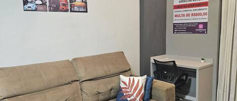 Un salón con sofá, un escritorio pequeño y una pared con un cartel de prohibido.