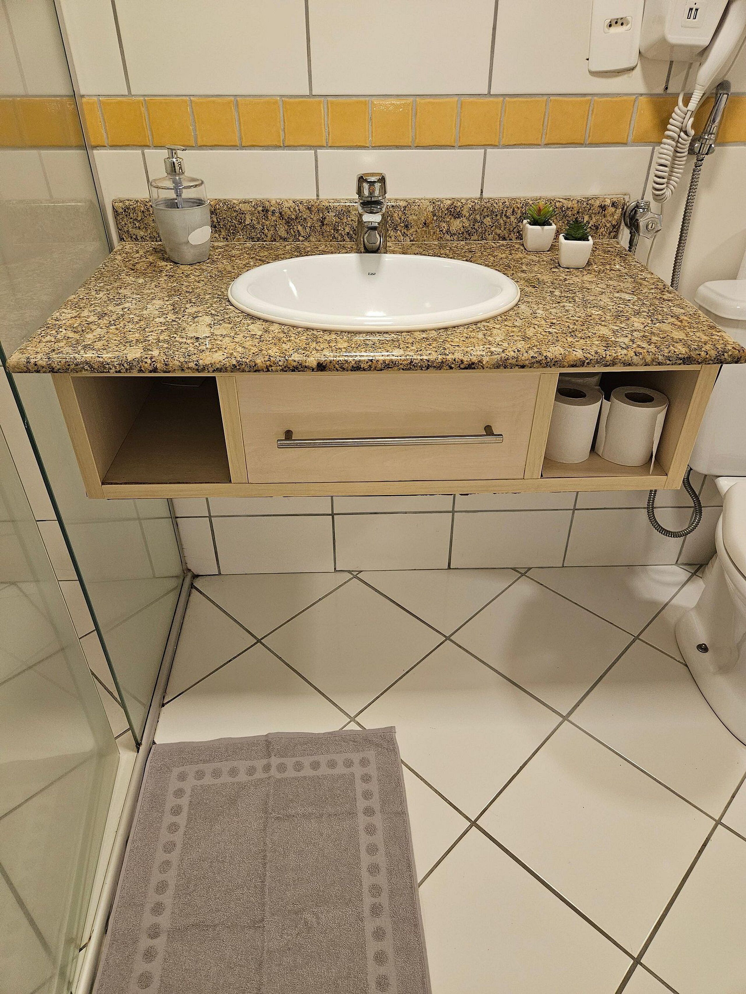 Um banheiro com bancada de granito, pia branca, porta-toalhas e vaso sanitário.