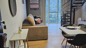 A modern living room with a sofa, a dining table, and a staircase. - Saint Sebastian Flat 716Duplex no Centro (Jaragua do Sul)