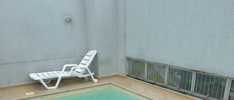 Una piscina rectangular con una tumbona blanca.