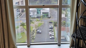 A room with a large window overlooking a parking area and a building with a green roof. - Saint Sebastian Flat 716Duplex no Centro (Jaragua do Sul)