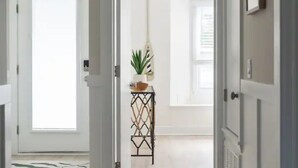 En gang med en hvid dør, et lille bord med en plante og en hængende lampe.