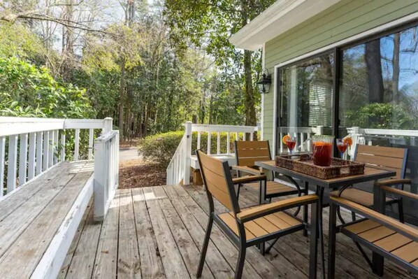 A wooden deck with a table and chairs, surrounded by a white railing, overlooking a forested area.