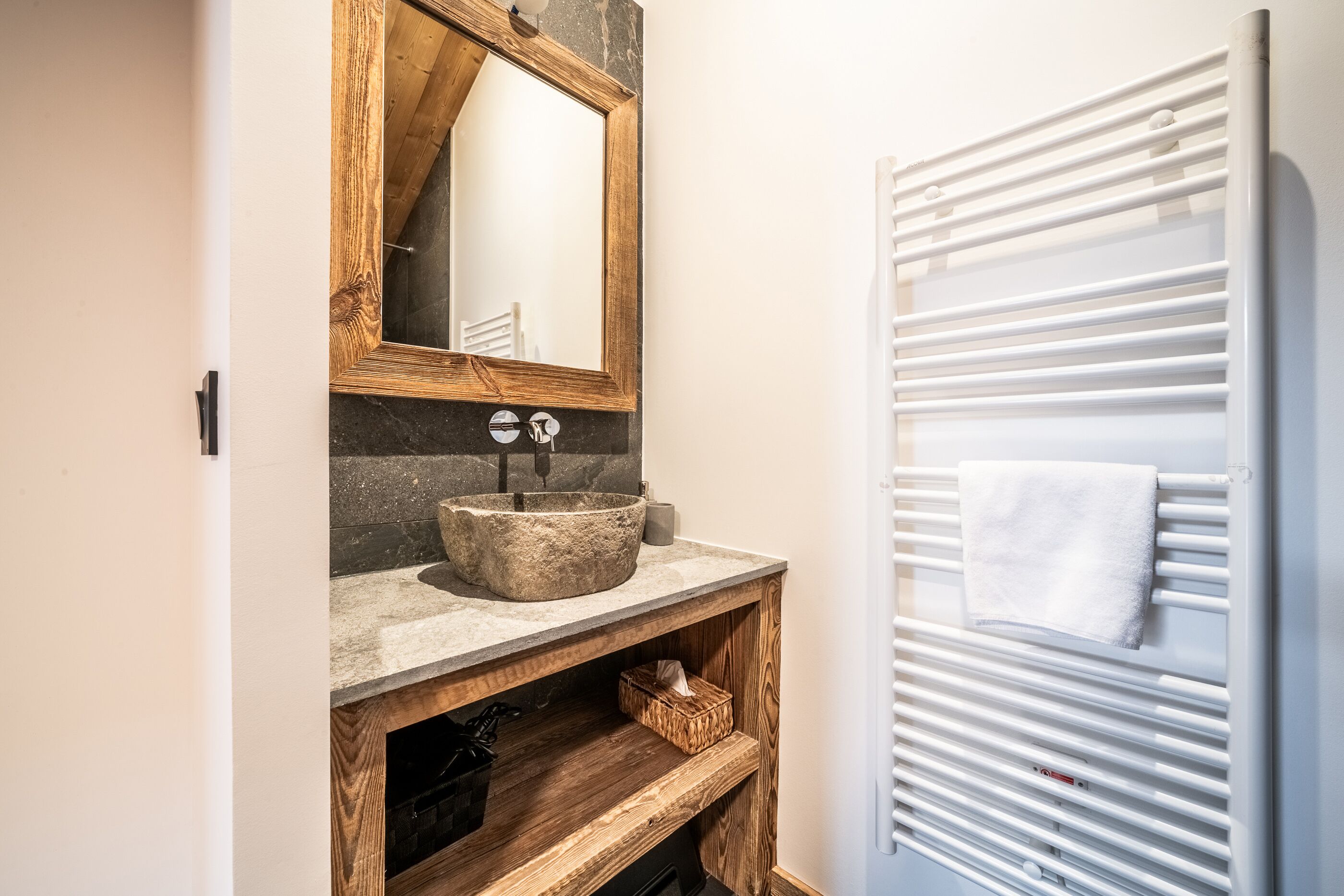 A bathroom with a stone sink, wooden shelves, a mirror, and a towel rack.