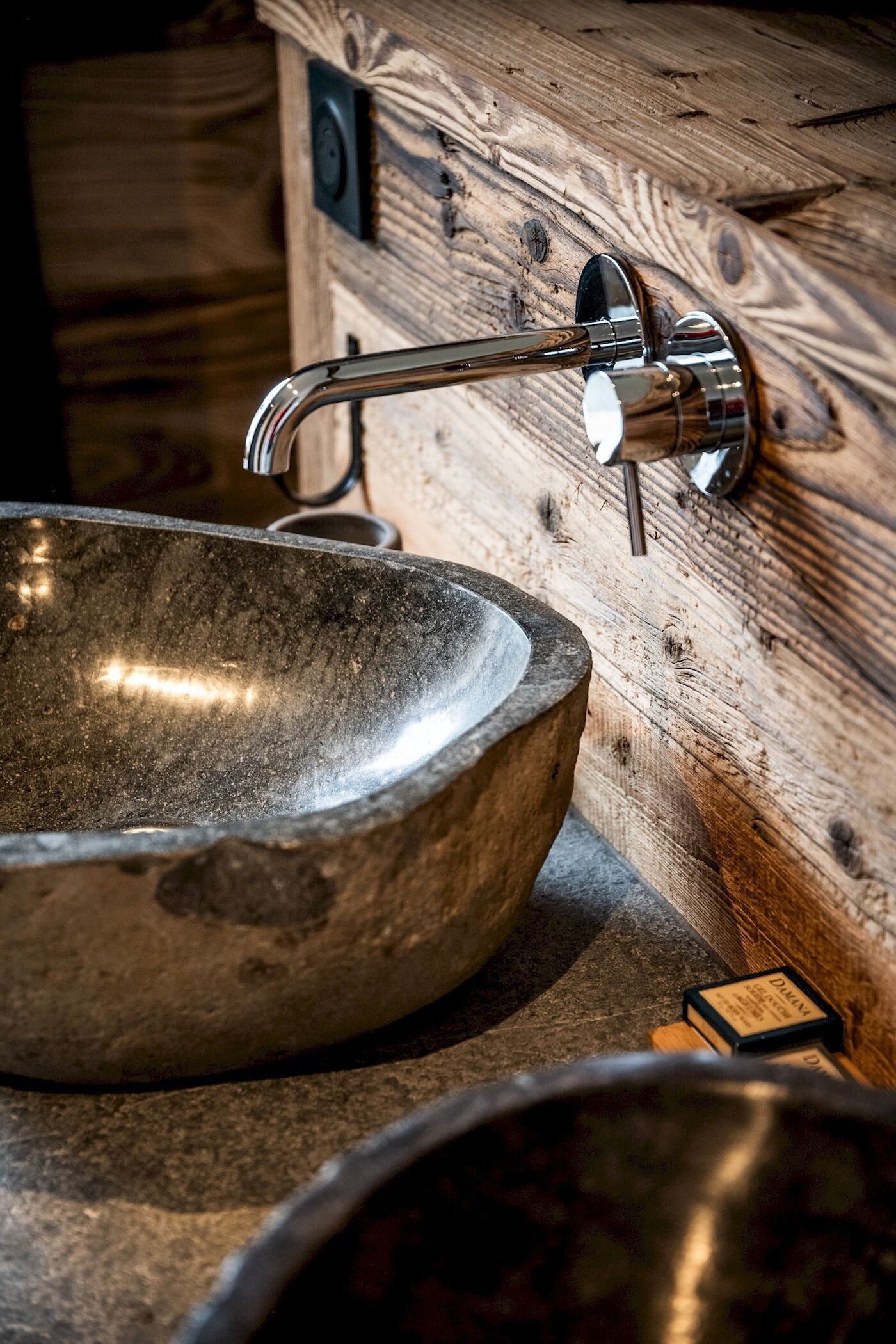 A stone sink with a modern faucet in a rustic setting.