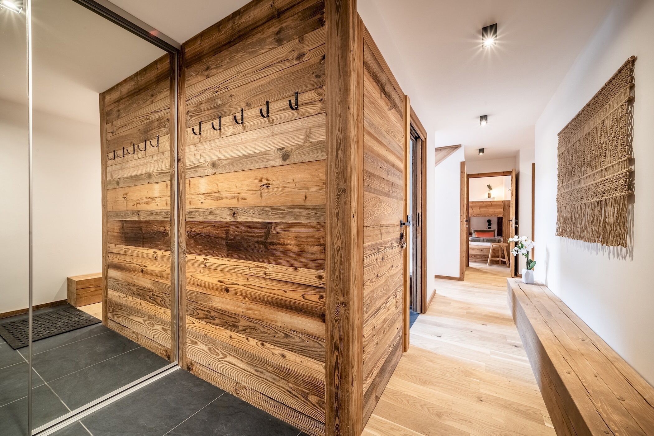 A wooden sliding door with the name "JUDD" carved into it, leading to a room with a bench and a wall-mounted macrame piece.