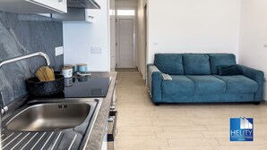 A modern kitchen with a stainless steel sink, a black countertop, and a blue sofa in the living area. - [Tropea] Luxury Terrace Sea suite ⭐️⭐️⭐️⭐️⭐️ (Tropea)