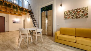 Un intérieur moderne avec un escalier, un coin repas avec des chaises, un canapé et un mur orné d’un tableau floral.