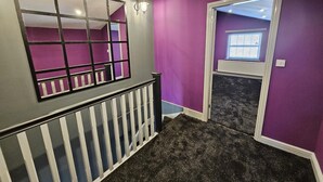 Ein Flur mit violetten Wänden, einer weißen Geländer und einem Fenster mit Jalousien.