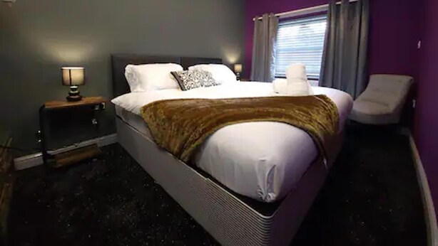 Ein Hotelzimmer mit einem Bett, einem Nachttisch, einem Sessel und einem Fenster mit Vorhängen.