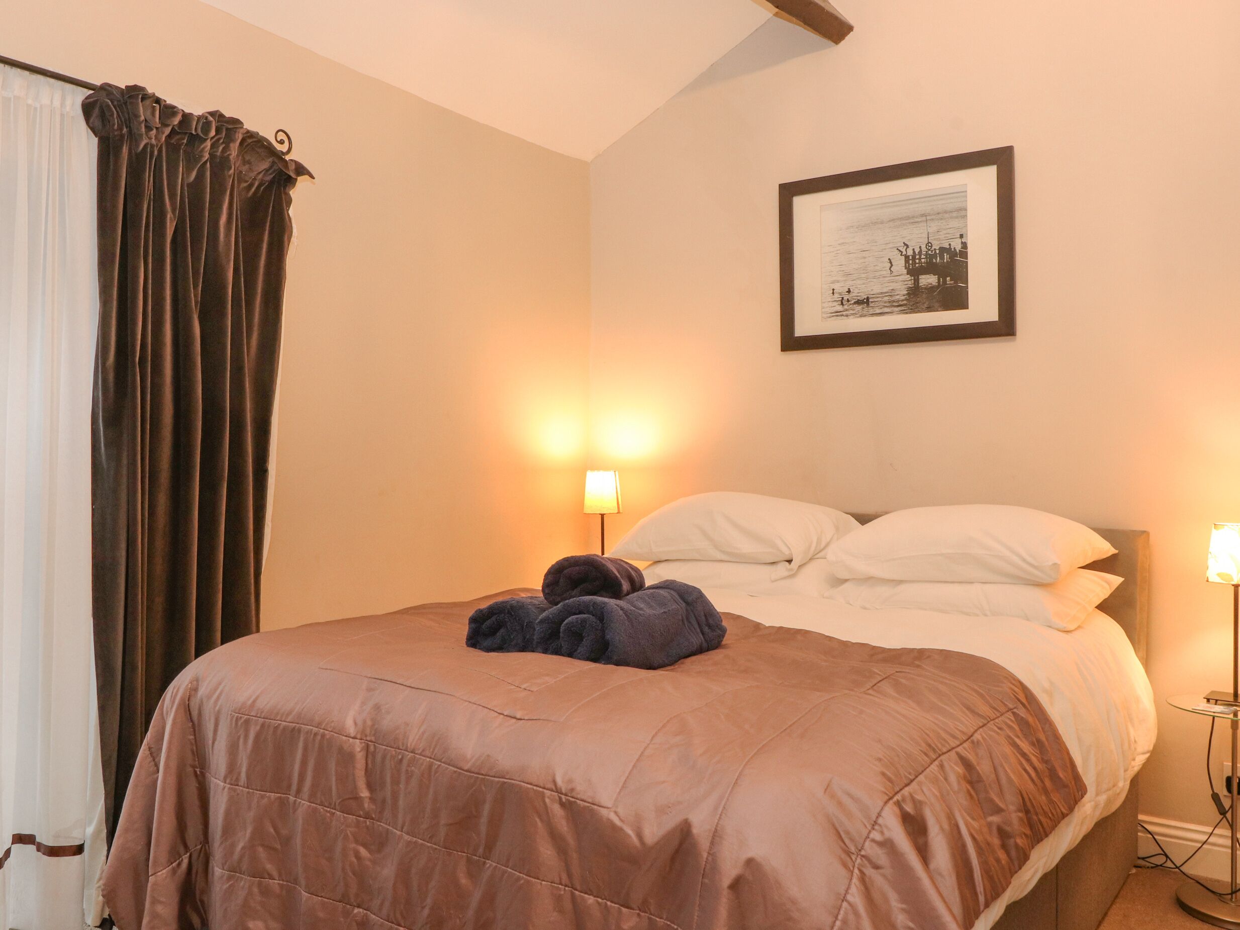 Una habitación de hotel con una cama, dos lámparas de noche, un cuadro en la pared y una cortina.