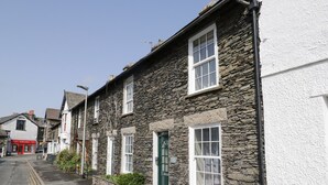 A row of stone buildings with white walls and green doors, a clear sky, and a street with double yellow lines. - Myrtle Cottage (Windermere)