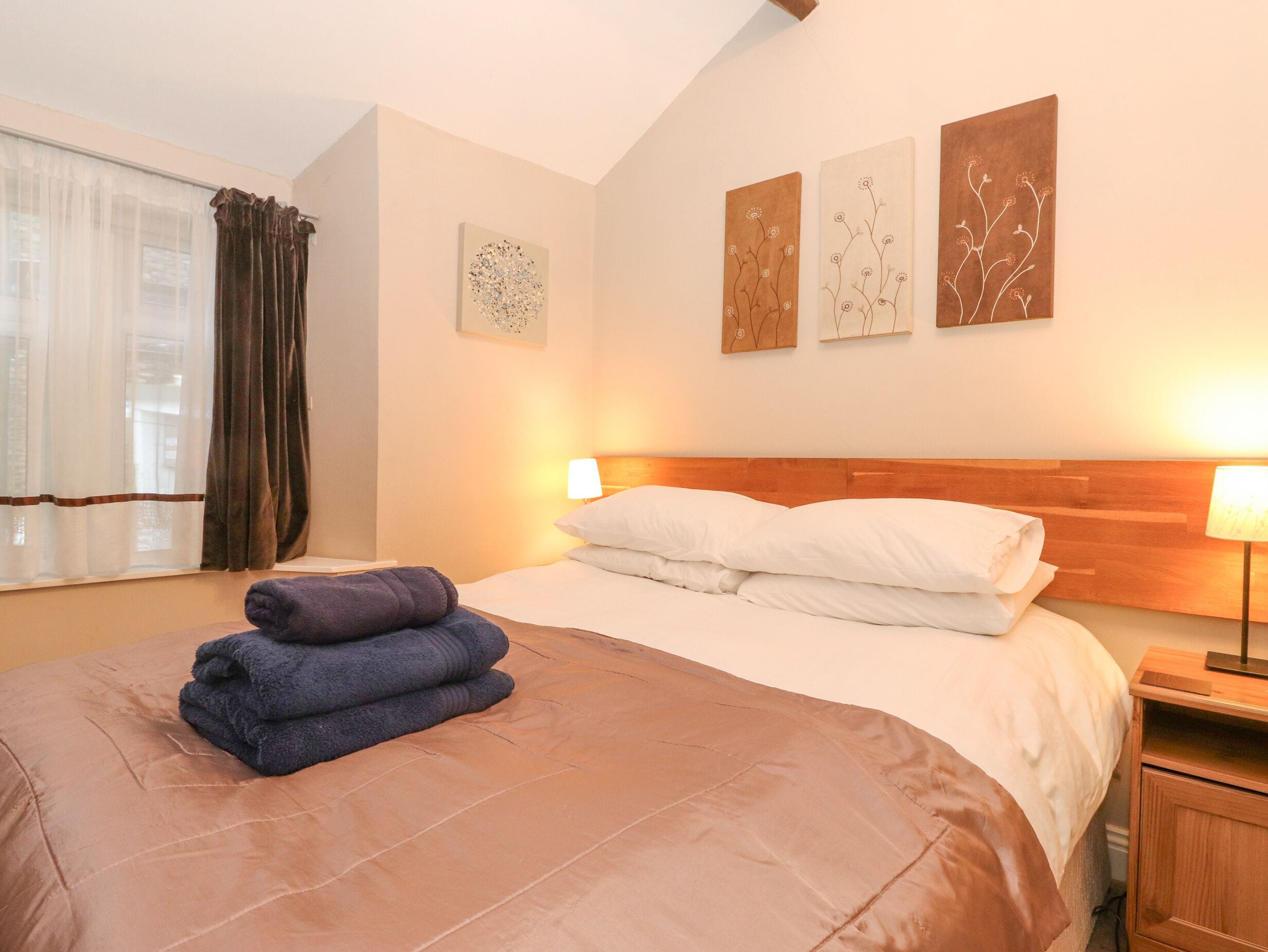 A hotel room with a bed, a window with curtains, and three wall-mounted artworks.