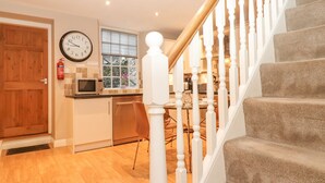 A kitchen with a microwave, a clock, and a window with blinds. - Myrtle Cottage (Windermere)