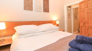 A neatly made bed with white linens, a wooden headboard, and a bedside lamp. There are three wall-mounted artworks above the bed. - Myrtle Cottage (Windermere)