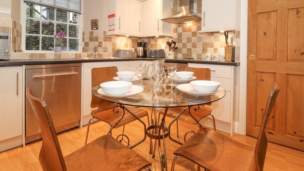 A modern kitchen with a glass dining table, white cabinets, and stainless steel appliances. - Myrtle Cottage (Windermere)