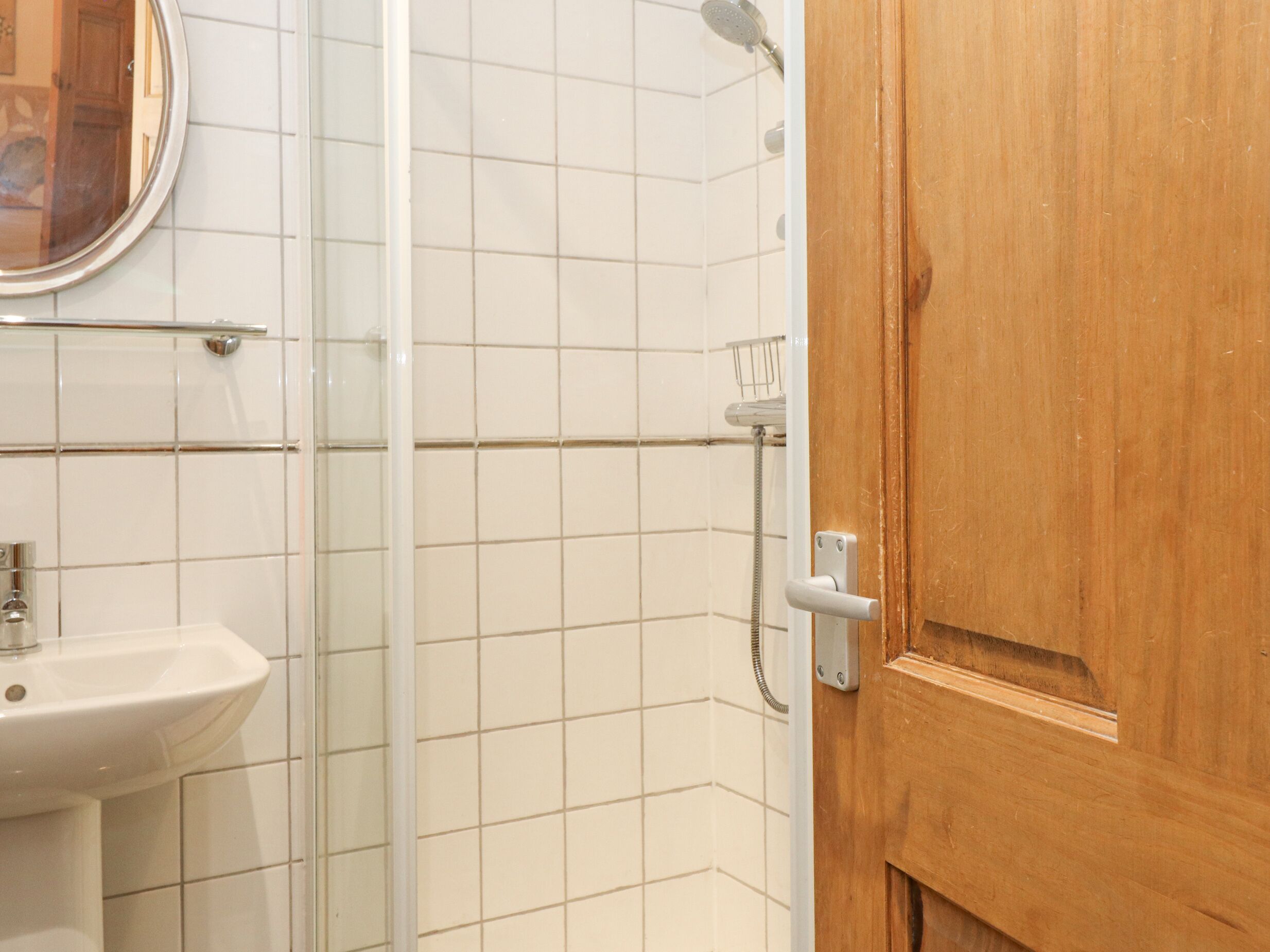 A bathroom with a sink, a shower, and a wooden door.