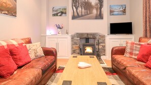A cozy living room with leather sofas, a fireplace, and artwork on the walls. - Myrtle Cottage (Windermere)